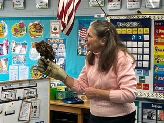 woman in pink shirts holding a small owl on her arm in a first grade classroom