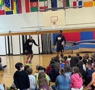Two basketball players dress in black  show tricks to students in the school gymnasium