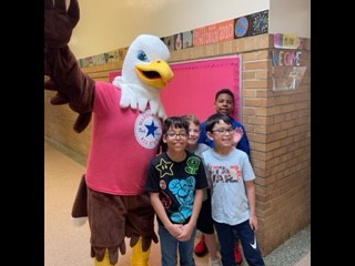 large mascot of an eagle stands in hallway with 4 students