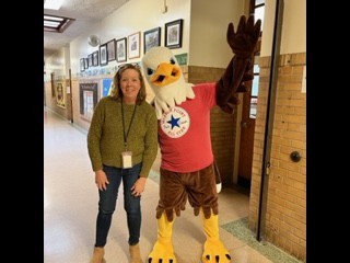 large eagle mascot in hallway with a 4th grade teacher dressed in denim with a green sweater