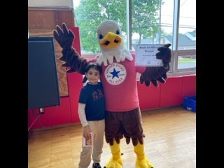 large eagle mascot stands in the school gymnasium with a 3rd grade students wearing brown and blue