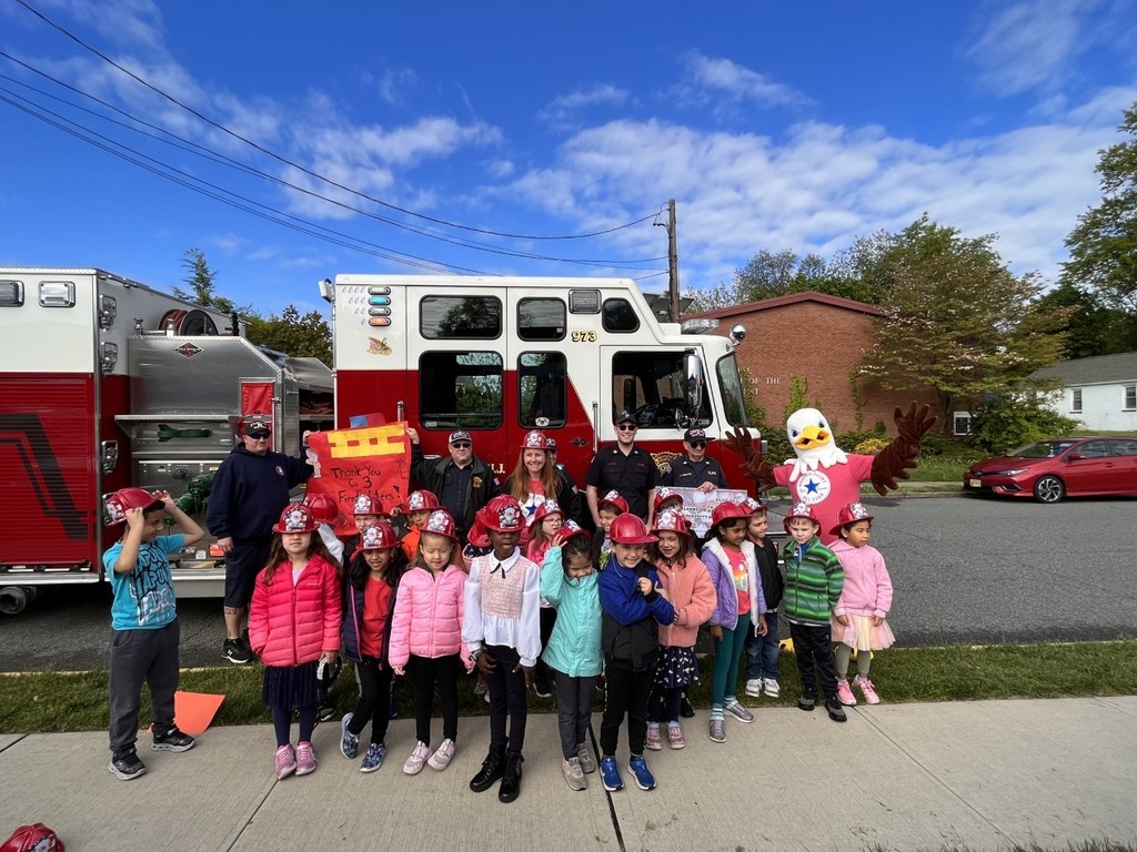 Kindergarten students, firefighters, and the school mascot Eagle standing outside of a red and white fire truck