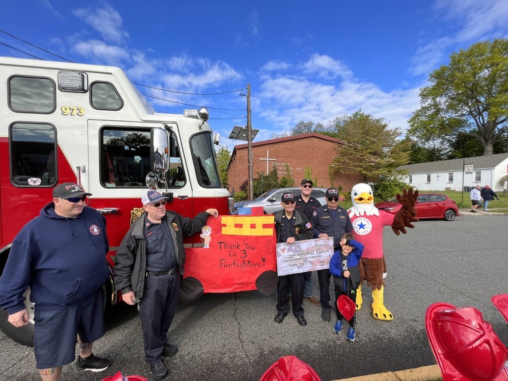Firefighters, a kindergarten student, and the school mascot Eagle stand outside of a red and white fire truck holding posters