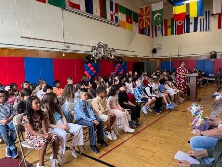 85 fourth graders and their teachers sitting in seats in the school gymnasium as Principal Gons opens the graduation ceremony